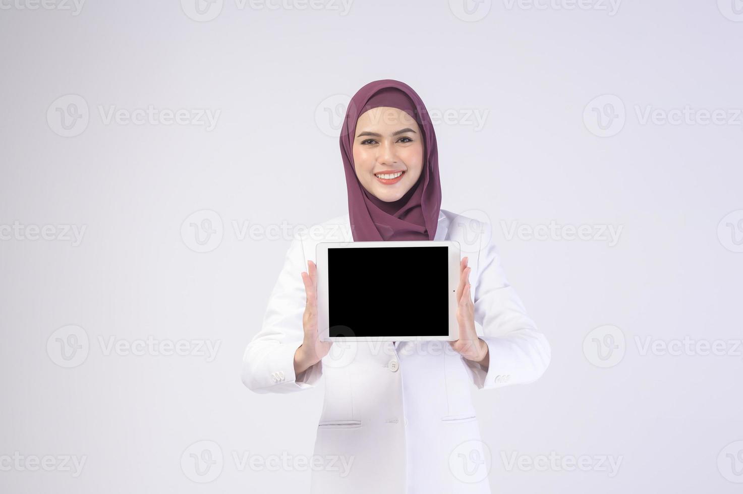 mooie moslim zakenvrouw die wit pak draagt met hijab die tablet in studio houdt foto