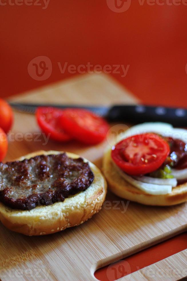 de Hamburger is wezen bereid en geserveerd met gesneden tomaten, uien, augurken. Aan een houten snijdend bord in de keuken foto