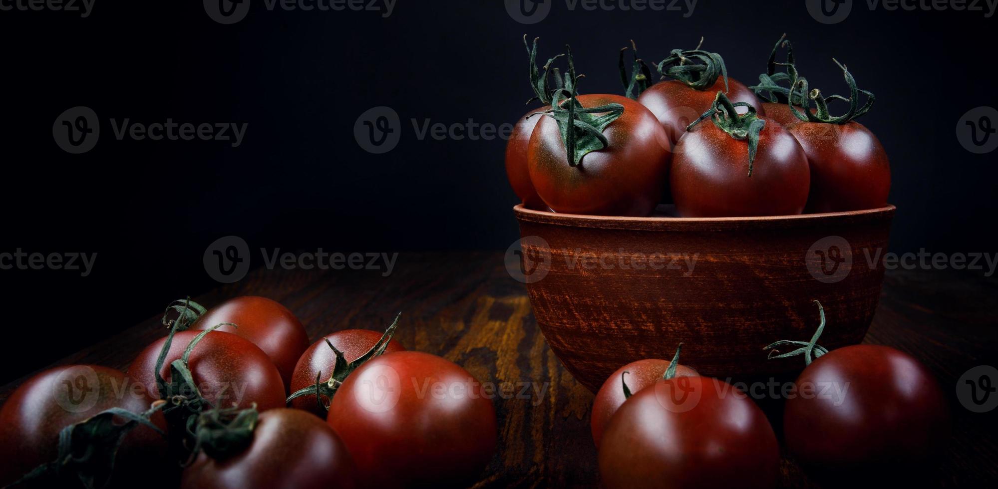 rijp sappig tomaten in een klei bord en De volgende naar het Aan een zwart achtergrond. foto