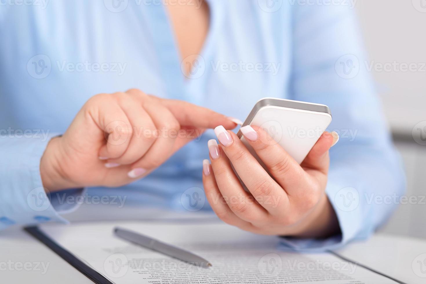 jonge vrouw die werkt met een mobiele telefoon boven het contract foto