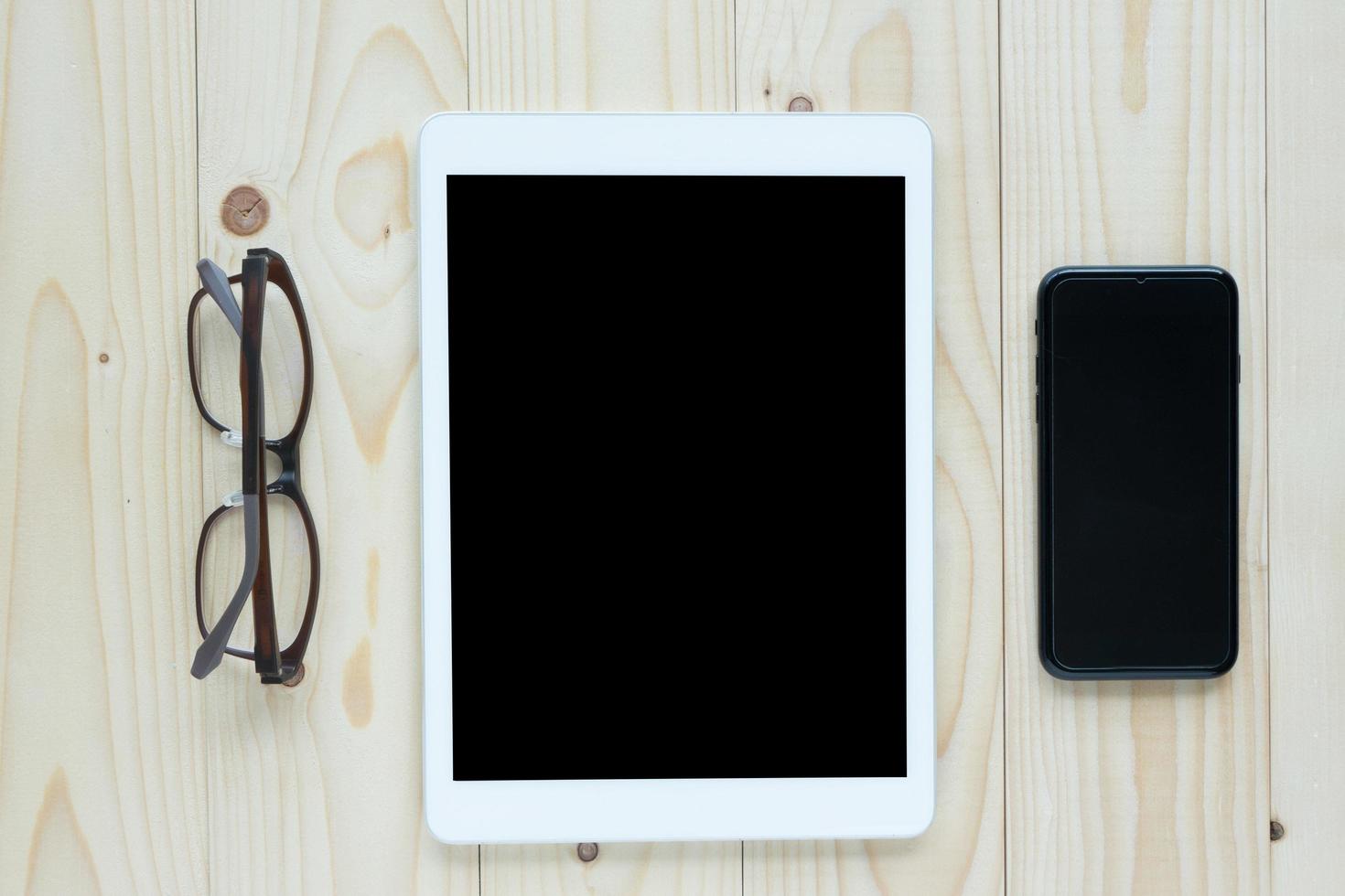 top visie van wit tablet blanco zwart scherm voor advertentie Scherm of andere app ontwerp met smartphone, koffie kop en bril Aan hout achtergrond foto