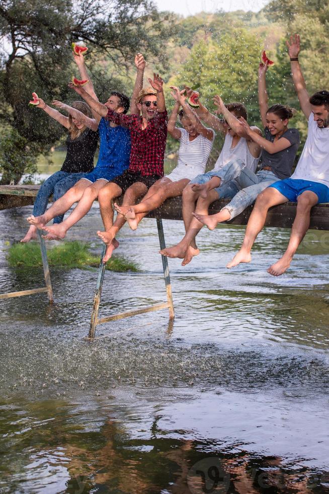 vrienden genieten van watermeloen terwijl zittend Aan de houten brug foto