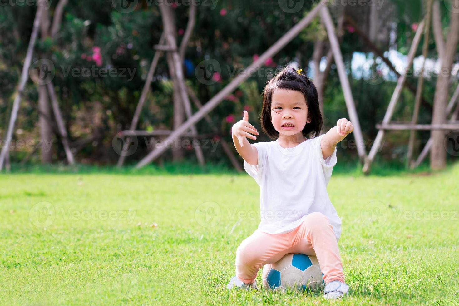 portret beeld van 4 baby kind. gelukkig Aziatisch kind meisje zittend Aan wit Blauw Amerikaans voetbal. kinderen gaf een duimen omhoog tonen dat het was groot. aan het leren sport en spelen concept. glimlachen weinig peuter. foto