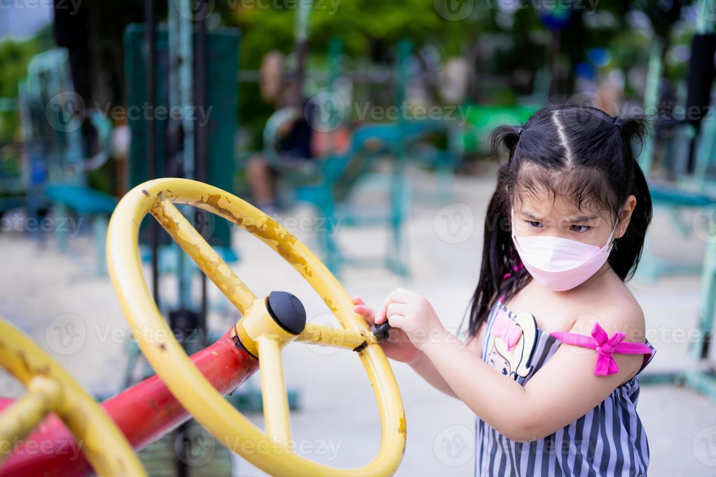 portret beeld kind 5-6 jaren oud. schattig meisje draagt masker terwijl spelen oefening uitrusting in park. kinderen zijn aan het leren interessant genoeg met speelplaats apparatuur. kind proberen naar beurt geel slingers. foto