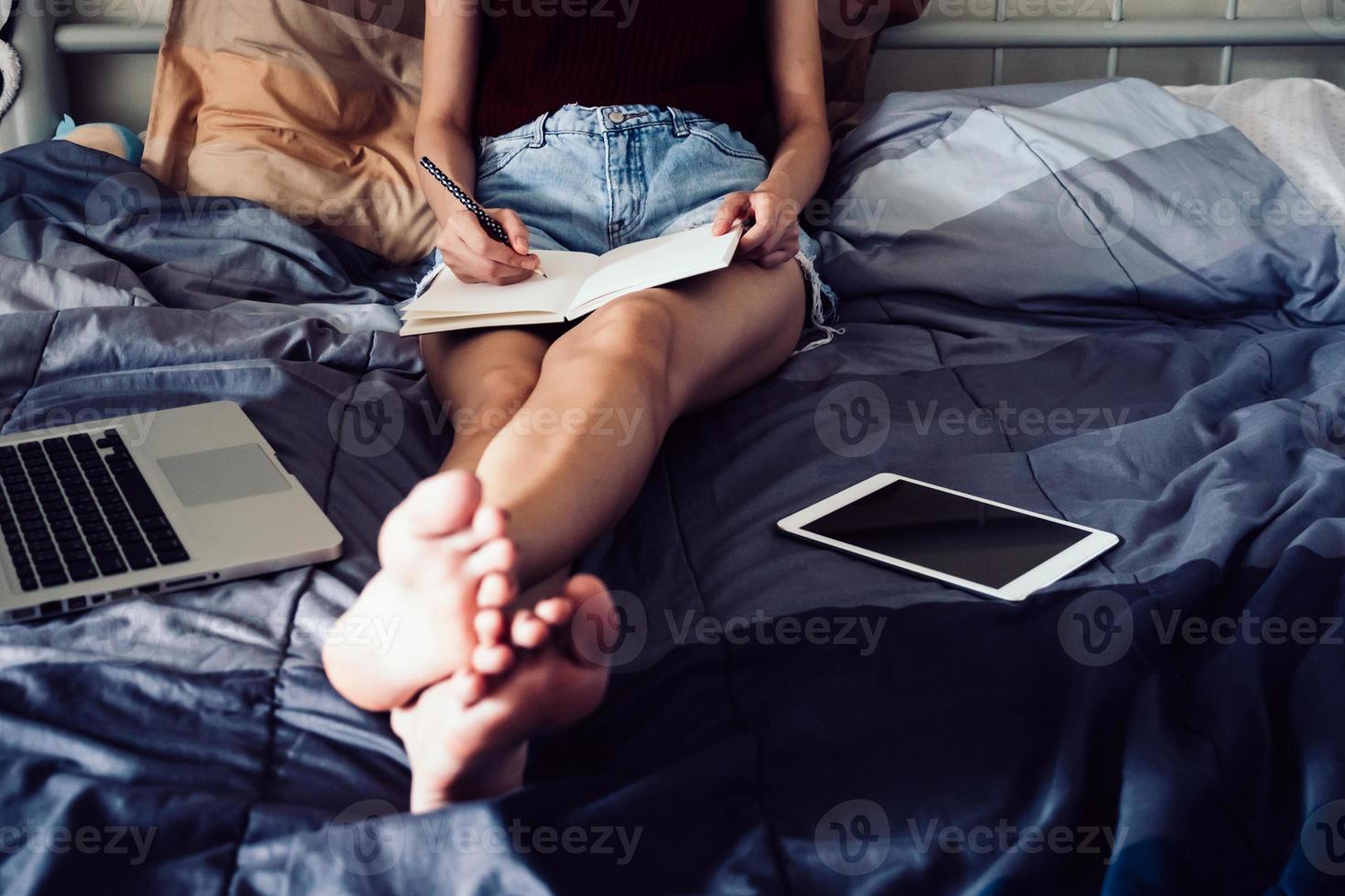 dichtbij omhoog van jong vrouw schrijven in een boek terwijl zittend Aan haar bed, films graan filter. foto