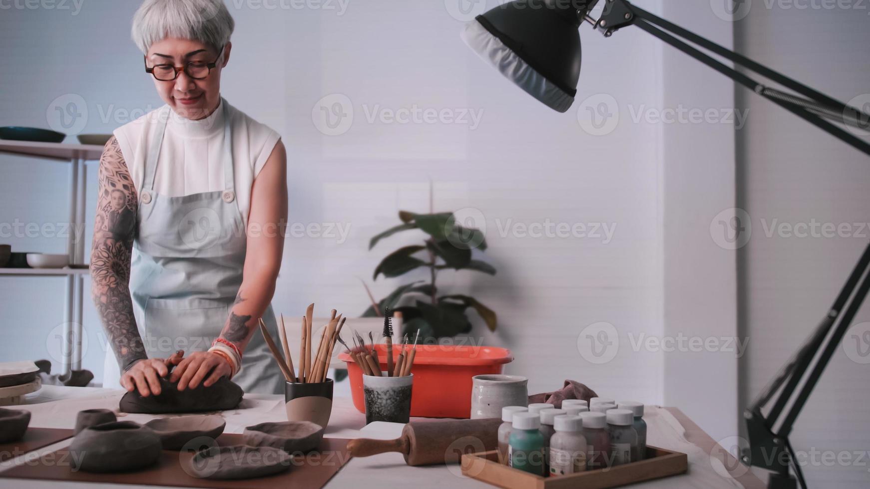 Aziatisch ouderen vrouw genieten van pottenbakkerij werk Bij huis. een vrouw keramist is maken nieuw pottenbakkerij in een studio. foto