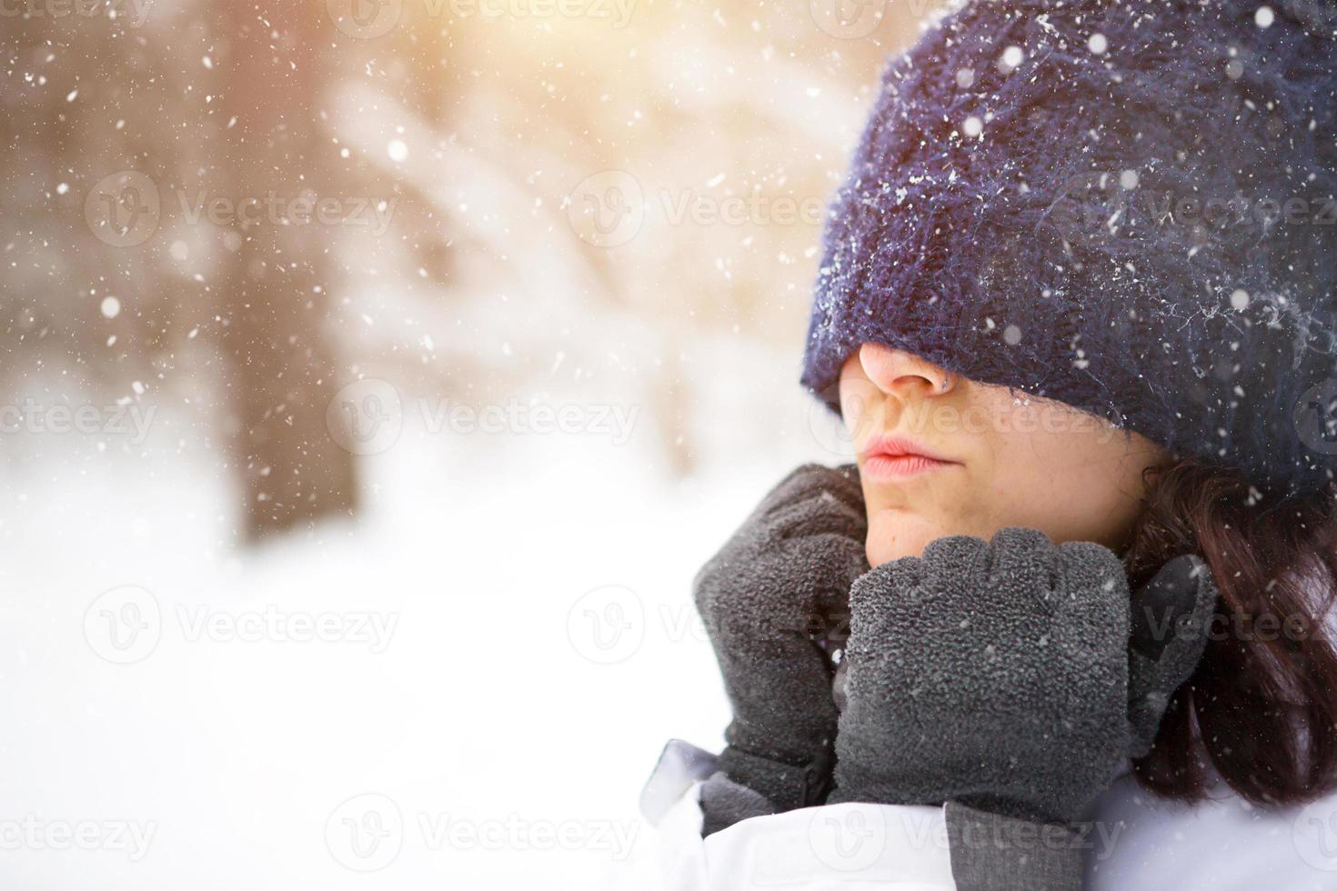 vrouw met gebreid hoed getrokken over- haar ogen verkoudheid en verwarmt haar handen met haar adem. buitenshuis activiteiten, voorjaar tijd, winter, sneeuw smelt, sneeuwval, vorst. schuilplaats van de het weer, comfort. detailopname foto