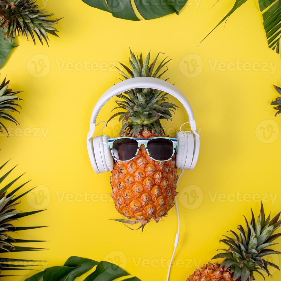 grappige ananas met witte hoofdtelefoon, luister muziek, geïsoleerd op gele achtergrond met tropische palmbladeren, bovenaanzicht, plat ontwerpconcept. foto