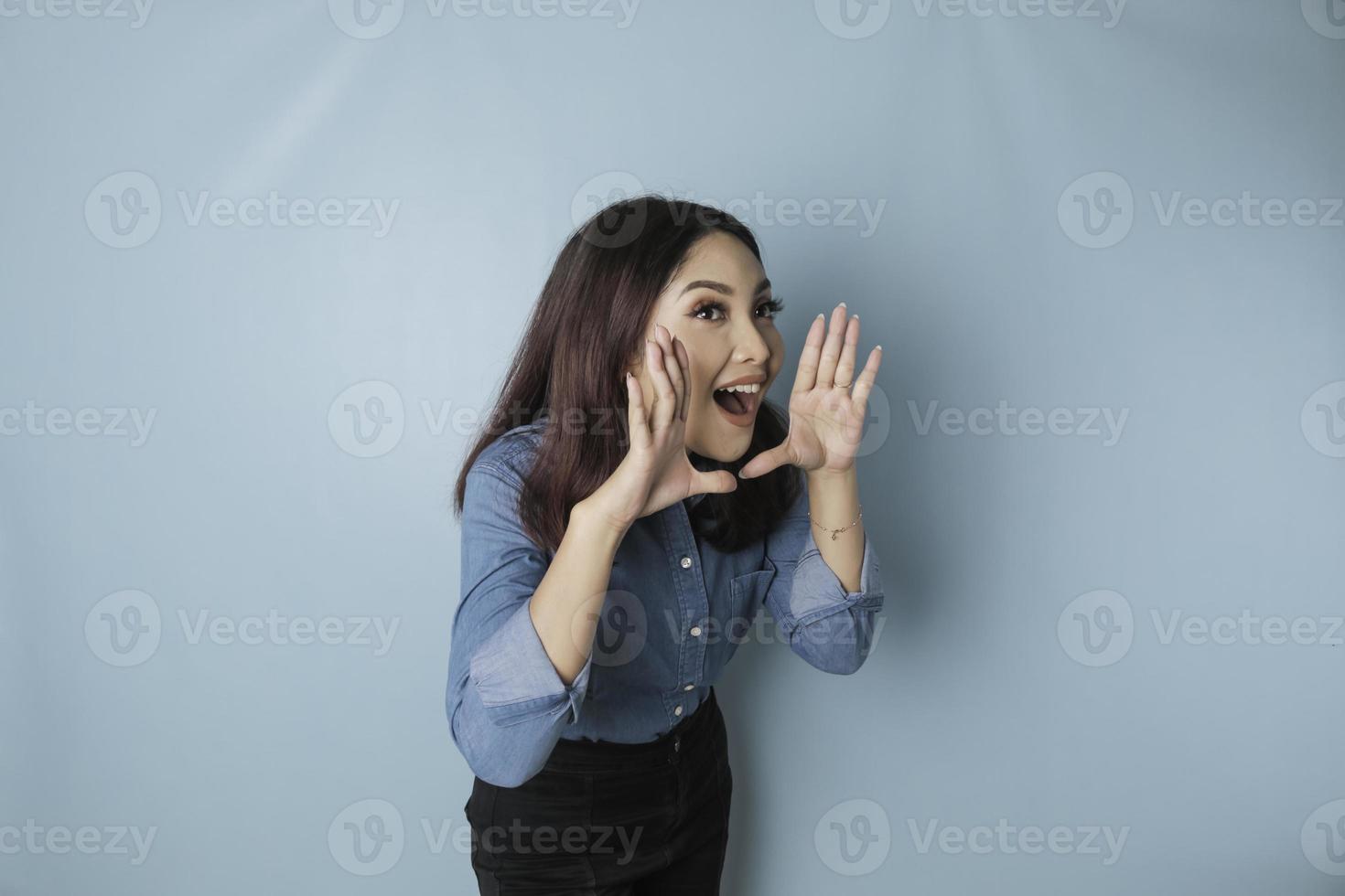 jong mooi vrouw vervelend een blauw overhemd geschreeuw en schreeuwen luid naar de kant met een hand- Aan haar mond. communicatie concept. foto