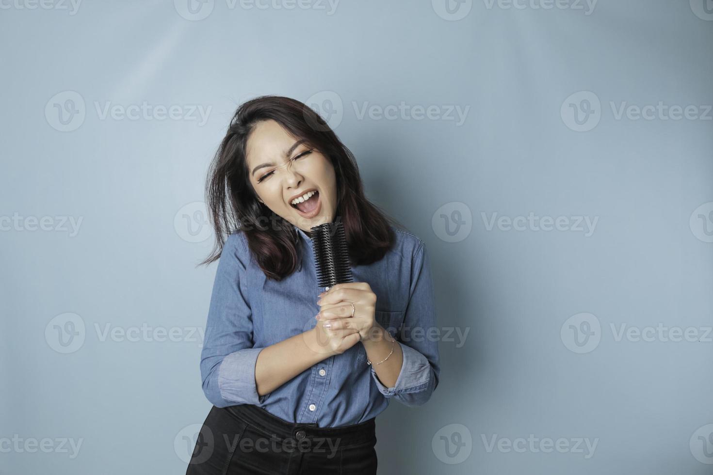 portret van zorgeloos Aziatisch vrouw, hebben pret karaoke, het zingen in microfoon terwijl staand over- blauw achtergrond foto