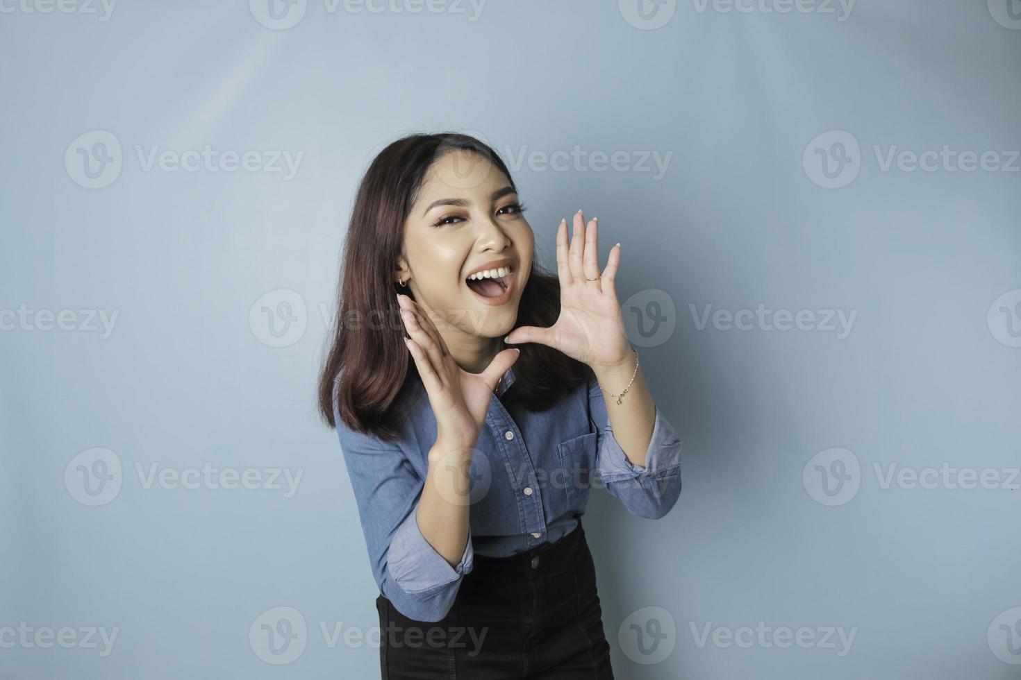 jong mooi vrouw vervelend een blauw overhemd geschreeuw en schreeuwen luid naar de kant met een hand- Aan haar mond. communicatie concept. foto