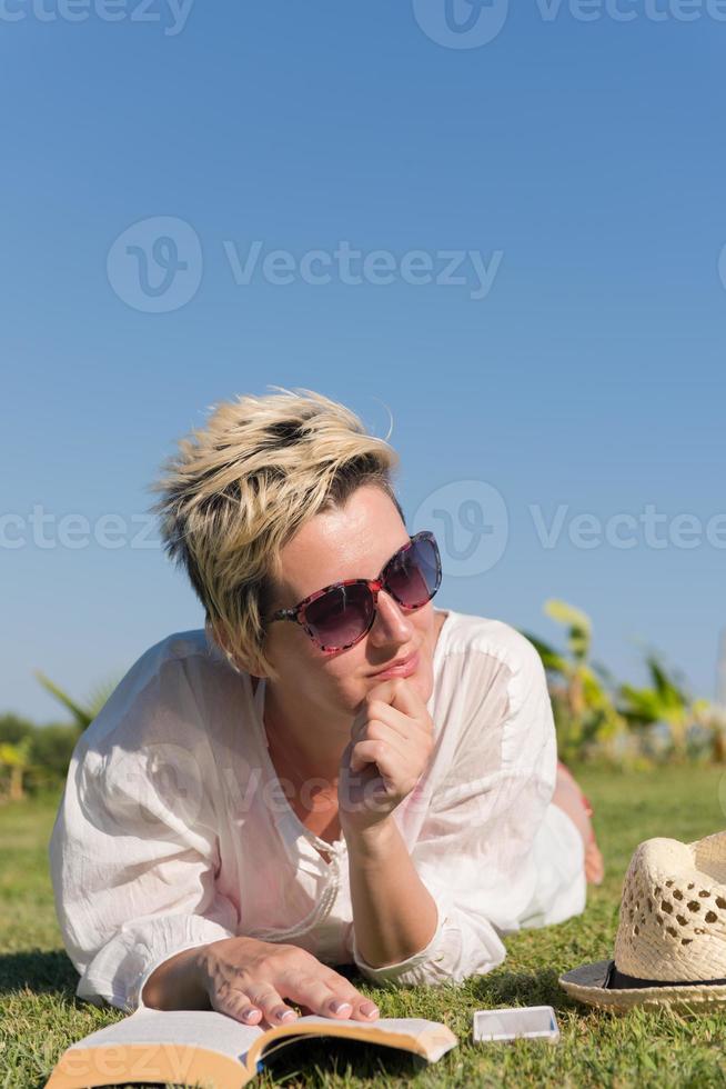 vrouw aan het liegen en lezing haar favoriete boek Aan een weide gedekt met vers groen gras Aan een zonnig zomer of voorjaar dag. foto