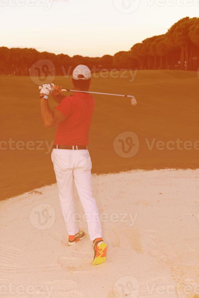 golfspeler raken een zand bunker schot Aan zonsondergang foto
