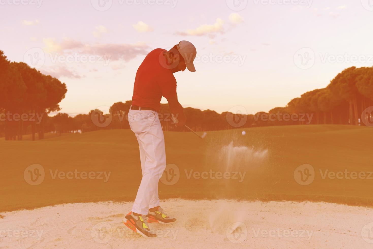 golfspeler raken een zand bunker schot Aan zonsondergang foto