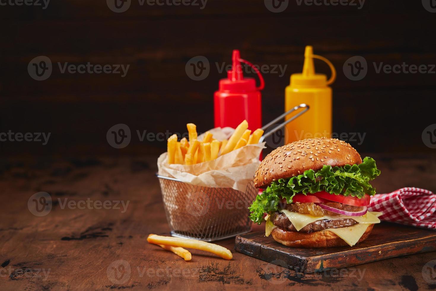 eigengemaakt hamburger met rundvlees, kaas en ui marmelade Aan een houten bord, Patat in een metaal mand en sauzen. snel voedsel concept, Amerikaans voedsel foto