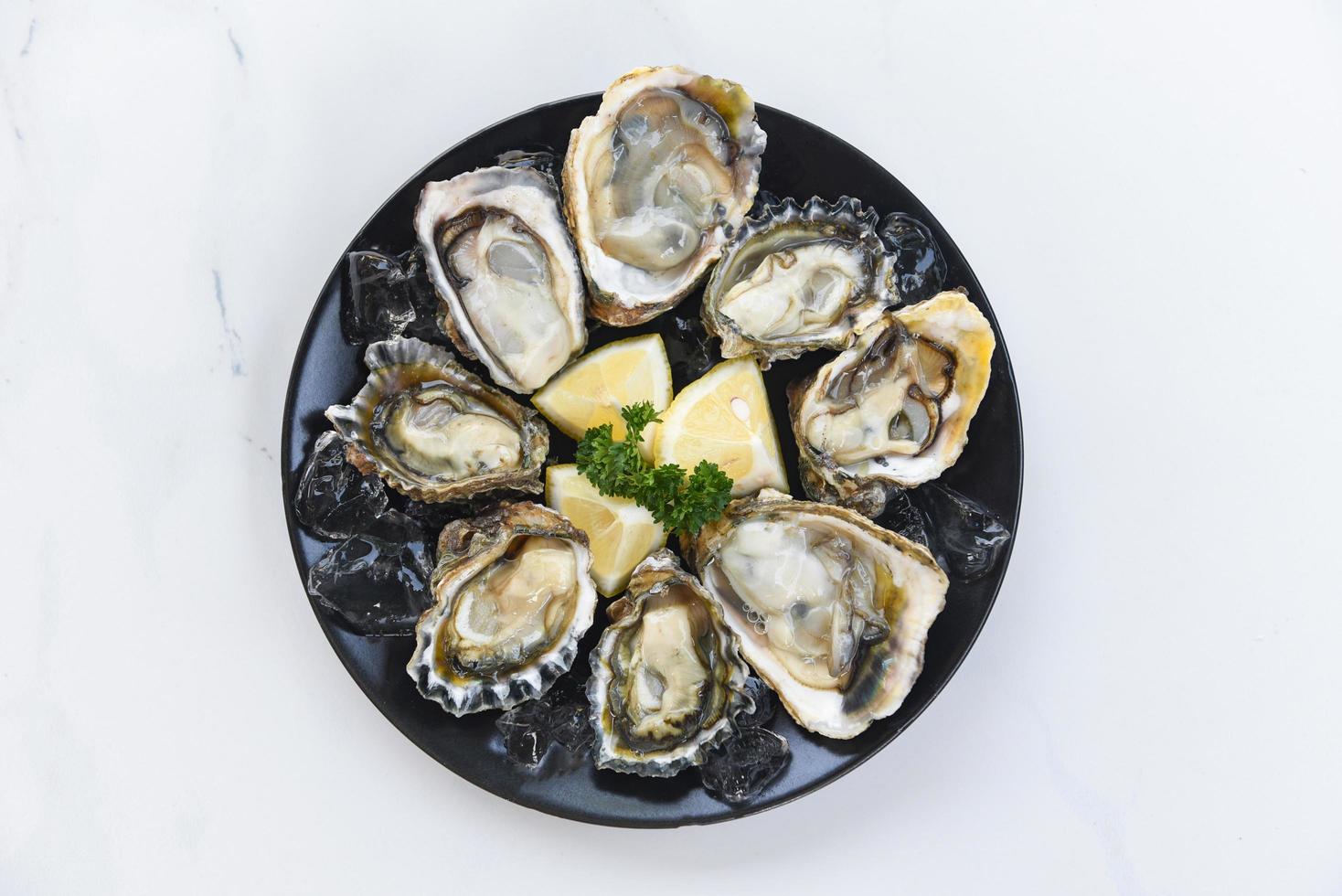 verse oesters zeevruchten op een zwarte plaat achtergrond - open oesterschelp met kruidenkruiden citroen rozemarijn geserveerd tafel en ijs gezonde zeevruchten rauwe oester diner in het restaurant gastronomische gerechten foto
