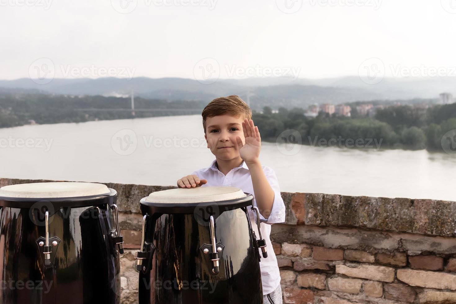 gelukkig jongen spelen conga instrument Bij rivieroever. foto