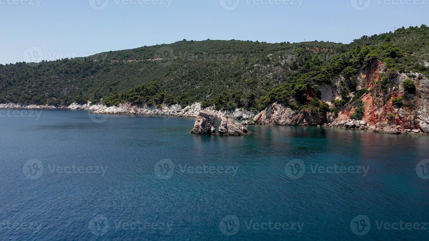 drone-uitzichten vanuit de lucht over een rotsachtige kustlijn, kristalhelder Egeïsch zeewater, toeristische stranden en veel groen op het eiland Skopelos, Griekenland. een typisch beeld van veel vergelijkbare Griekse eilanden. foto