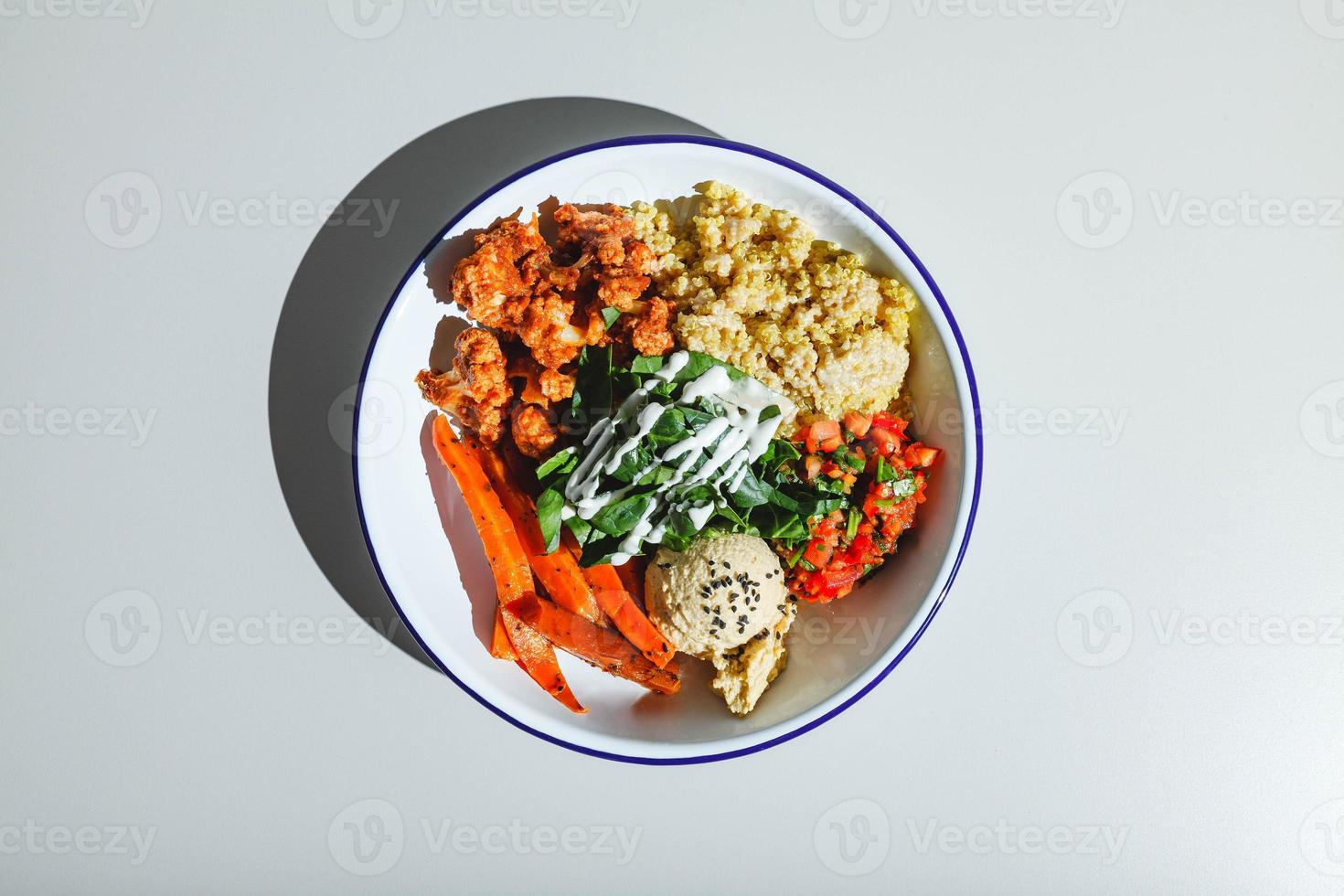 vegetarisch kom met quinoa, wortels, bloemkool in saus, spinazie, tomaten en hummus. moeilijk licht, diep schaduw foto