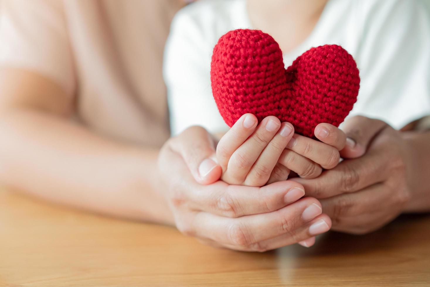 volwassen en kind handen Holding een garen rood hart. hoop, liefde, leven concept foto