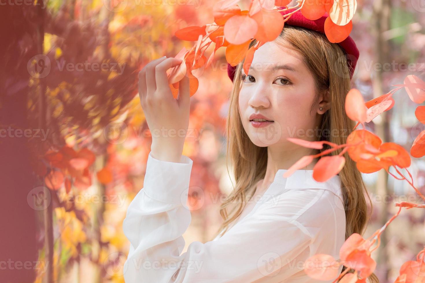 Aziatisch vrouw wie draagt wit overhemd en rood pet staat in rood oranje vertrekken net zo Forrest in herfst. foto