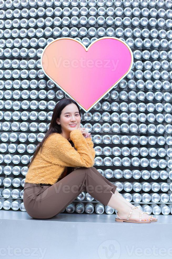 Aziatische mooie vrouw met lang haar zit en lacht op hart achtergrond als Valentijnsdag concept. abstracte achtergrond foto