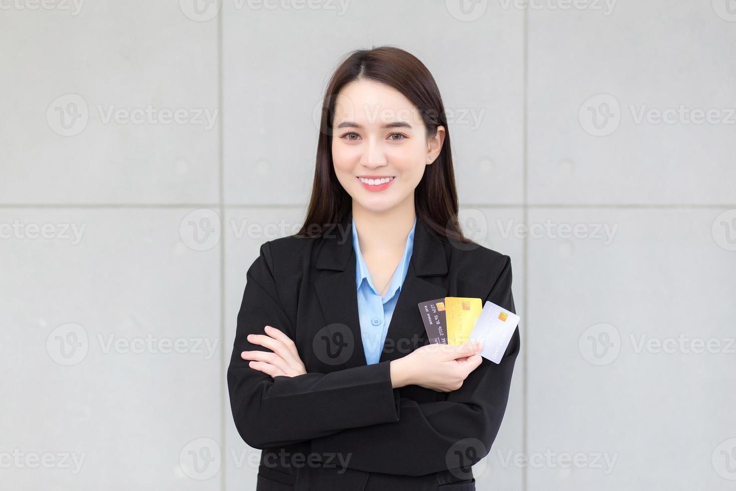 Aziatisch bedrijf vrouw in formeel zwart pak houdt en shows credit kaart in haar hand. financieel keuze concept. foto