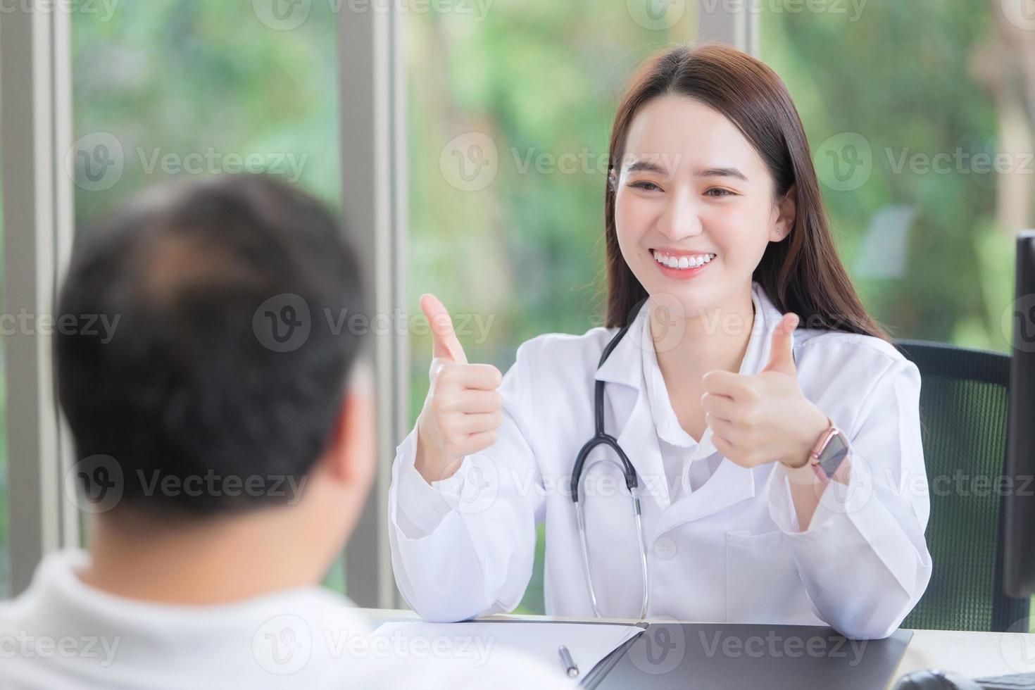 Aziatisch mooi vrouw dokter glimlacht en shows bonzen omhoog teken of heel mooi zo met haar geduldig ten gevolge naar zijn gezondheidszorg Bij ziekenhuis. foto