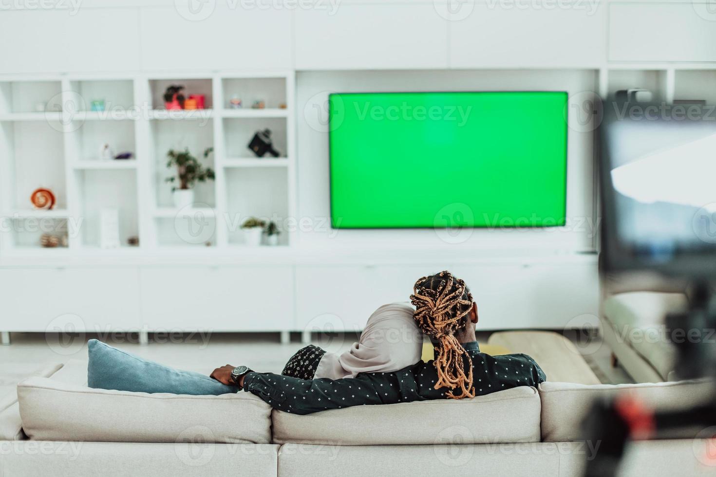 Afrikaanse paar zittend Aan sofa aan het kijken TV samen chroma groen scherm vrouw vervelend Islamitisch hijab kleren foto