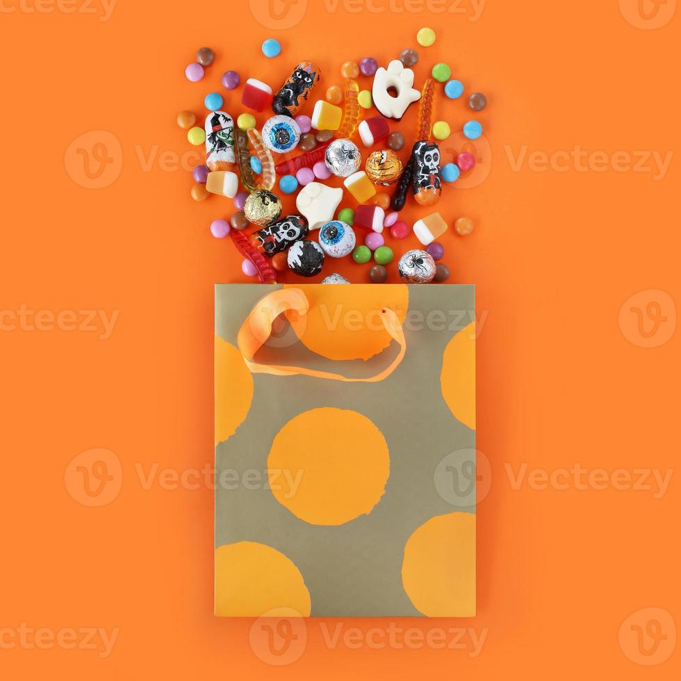 boodschappen doen papier oranje polka punt geschenk zak vol van gemorst geassorteerd traditioneel halloween snoepjes. oranje plein achtergrond met kopiëren ruimte. foto