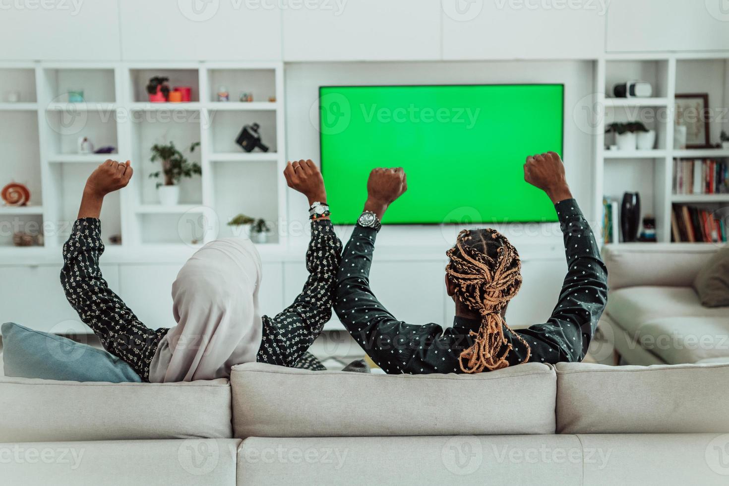 Afrikaanse paar zittend Aan sofa aan het kijken TV samen chroma groen scherm vrouw vervelend Islamitisch hijab kleren foto