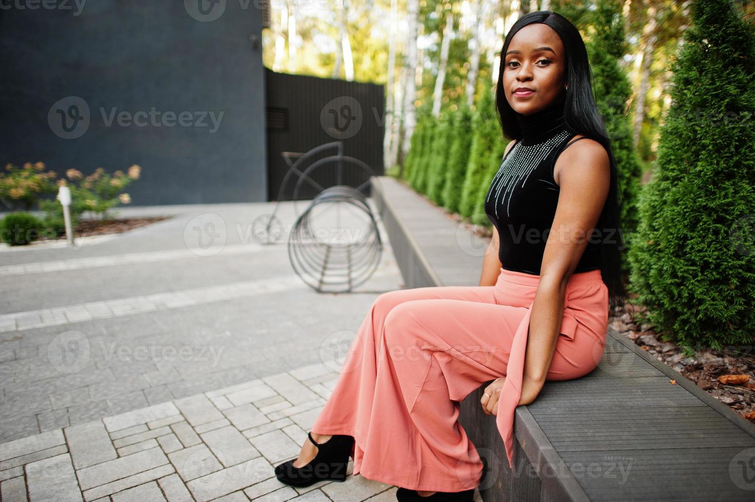 modieus Afrikaanse Amerikaans vrouw in perzik broek en zwart blouse houding buitenshuis. foto