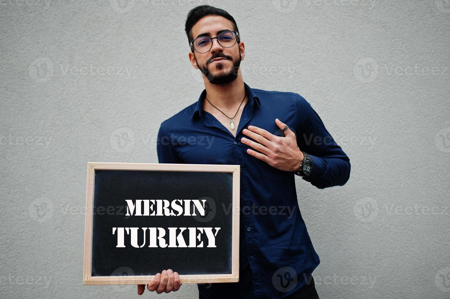 Arabisch Mens slijtage blauw overhemd en bril houden bord met mersin kalkoen inscriptie. grootste steden in Islamitisch wereld concept. foto