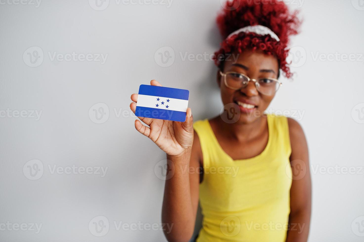 Afrikaanse Amerikaans vrouw met afro haar, slijtage geel singlet en bril, houden Honduras vlag geïsoleerd Aan wit achtergrond. foto