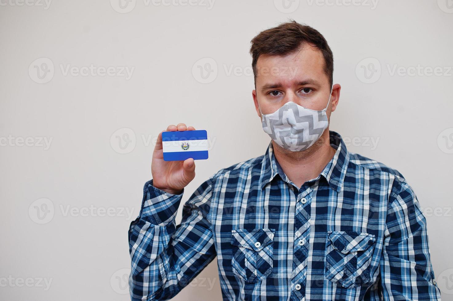 Mens in geruit overhemd tonen el Salvador vlag kaart in hand, slijtage beschermen masker geïsoleerd Aan wit achtergrond. Amerikaans landen coronavirus concept. foto