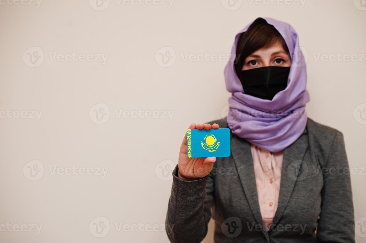 portret van jong moslim vrouw vervelend formeel dragen, beschermen gezicht masker en hijab hoofd sjaal, houden Kazachstan vlag kaart tegen geïsoleerd achtergrond. coronavirus land concept. foto