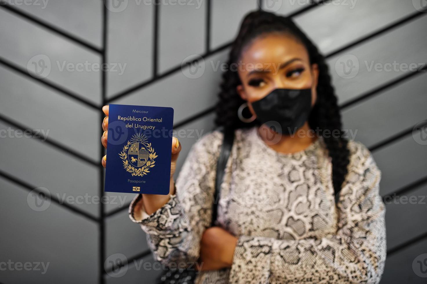 Afrikaanse Amerikaans vrouw vervelend zwart gezicht masker tonen Uruguay paspoort in hand. coronavirus in Amerika land, grens sluiting en quarantaine, virus het uitbreken concept. foto