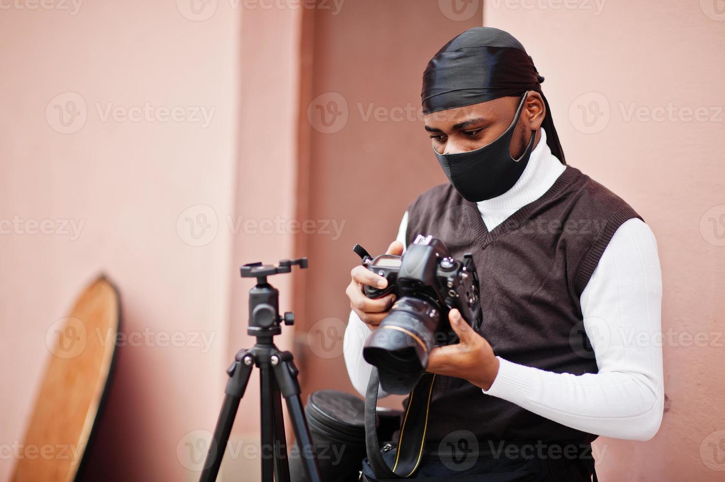 jong professioneel Afrikaanse Amerikaans videograaf Holding professioneel camera met pro apparatuur. afro cameraman vervelend zwart Duraq en gezicht beschermen masker, maken een videos. foto