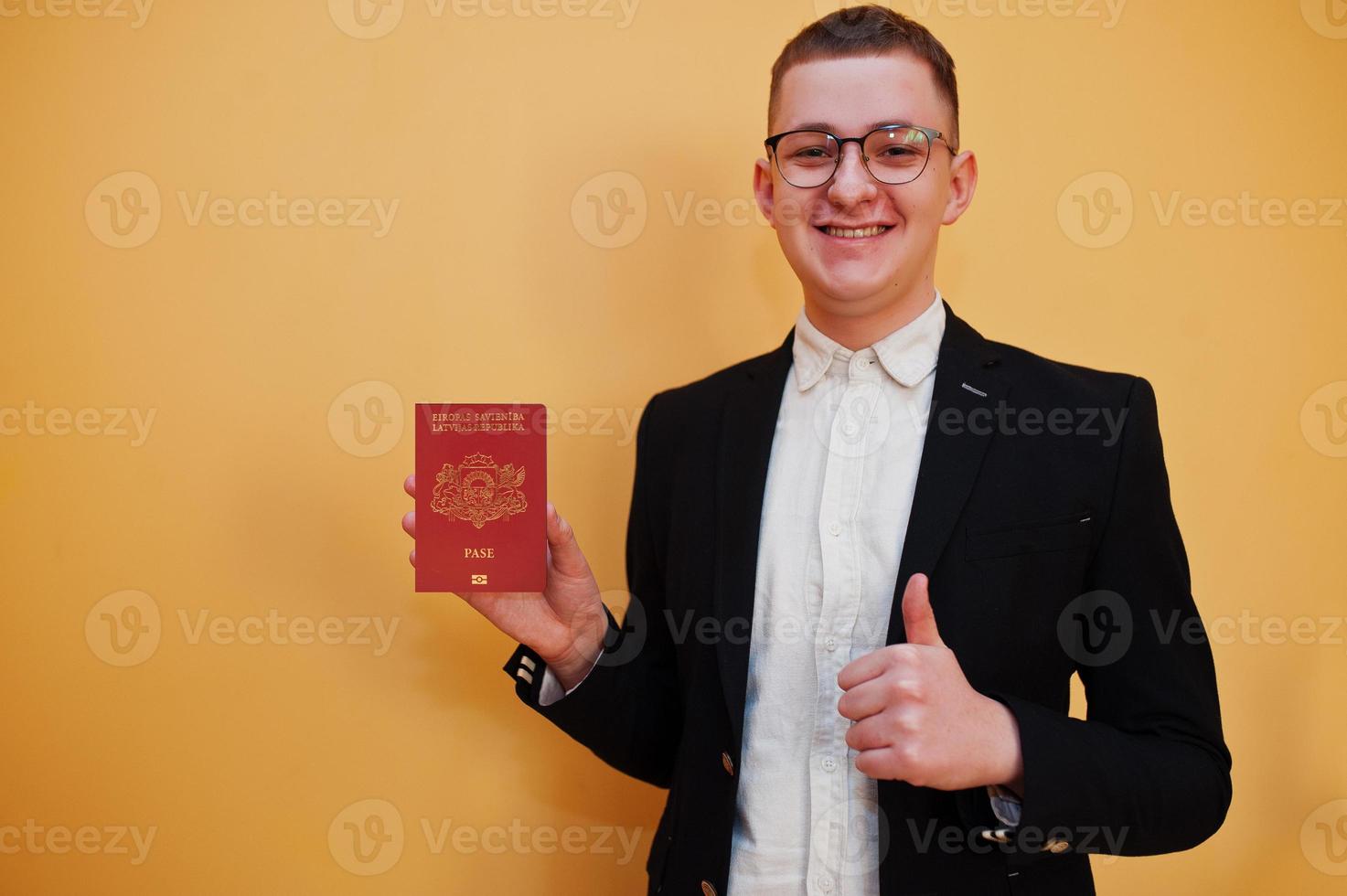 jong knap Mens Holding republiek van Letland paspoort ID kaart over- geel achtergrond, gelukkig en tonen duim omhoog. reizen naar Europa land concept. foto
