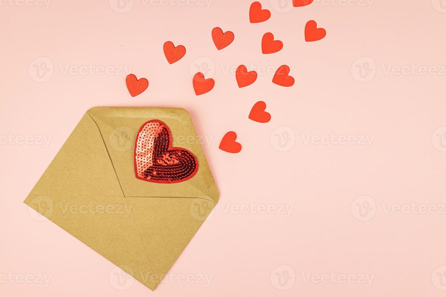 papier ambacht envelop met verstrooiing rood harten Aan roze achtergrond. met kopiëren ruimte. creatief lay-out voor st valentijnsdag dag. foto