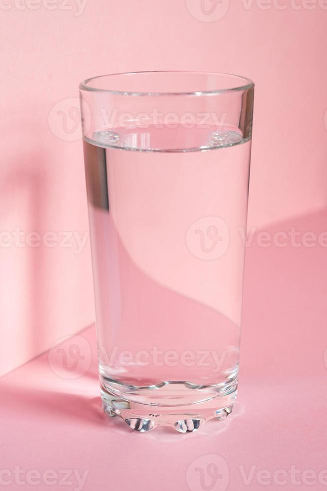 dichtbij omhoog van sprankelend water in transparant hoog glas en zon schittering Aan roze achtergrond foto