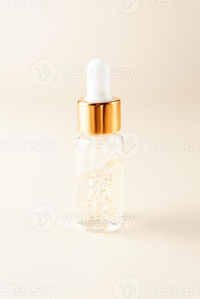 transparant fles met schoonheid serum, hyaluronzuur zuur, 24k goud en vitamines Aan een beige achtergrond. luxe huis gezicht en lichaam zorg behandeling concept. foto