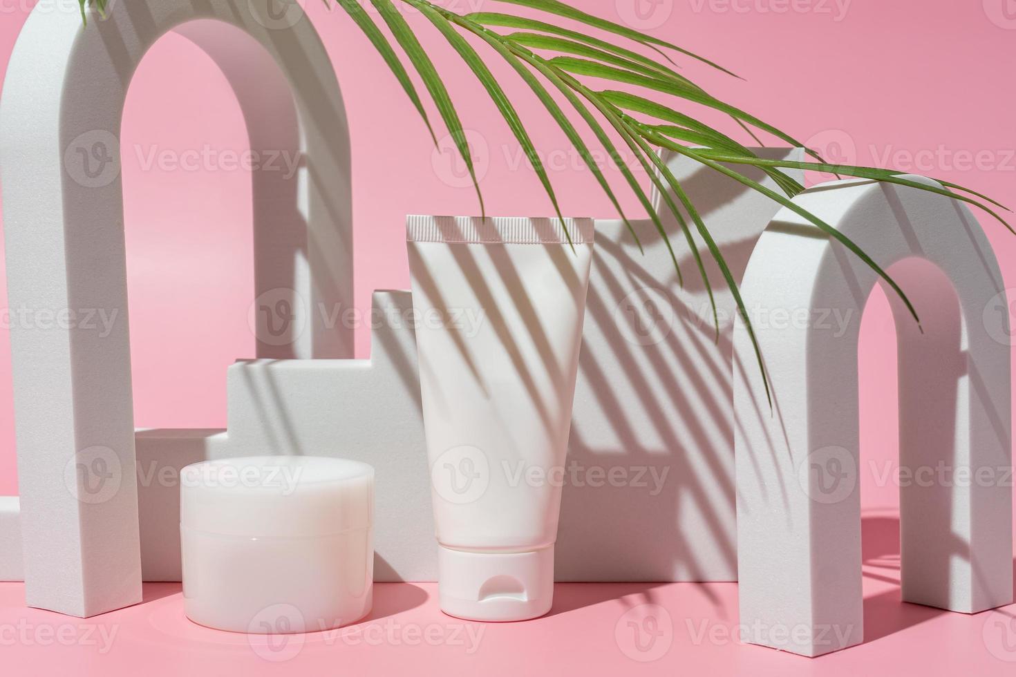 kunstmatig wit containers met palm blad Aan roze achtergrond. huid zorg producten. hand, gezicht, lichaam hydraterend room pot en plastic buis. foto