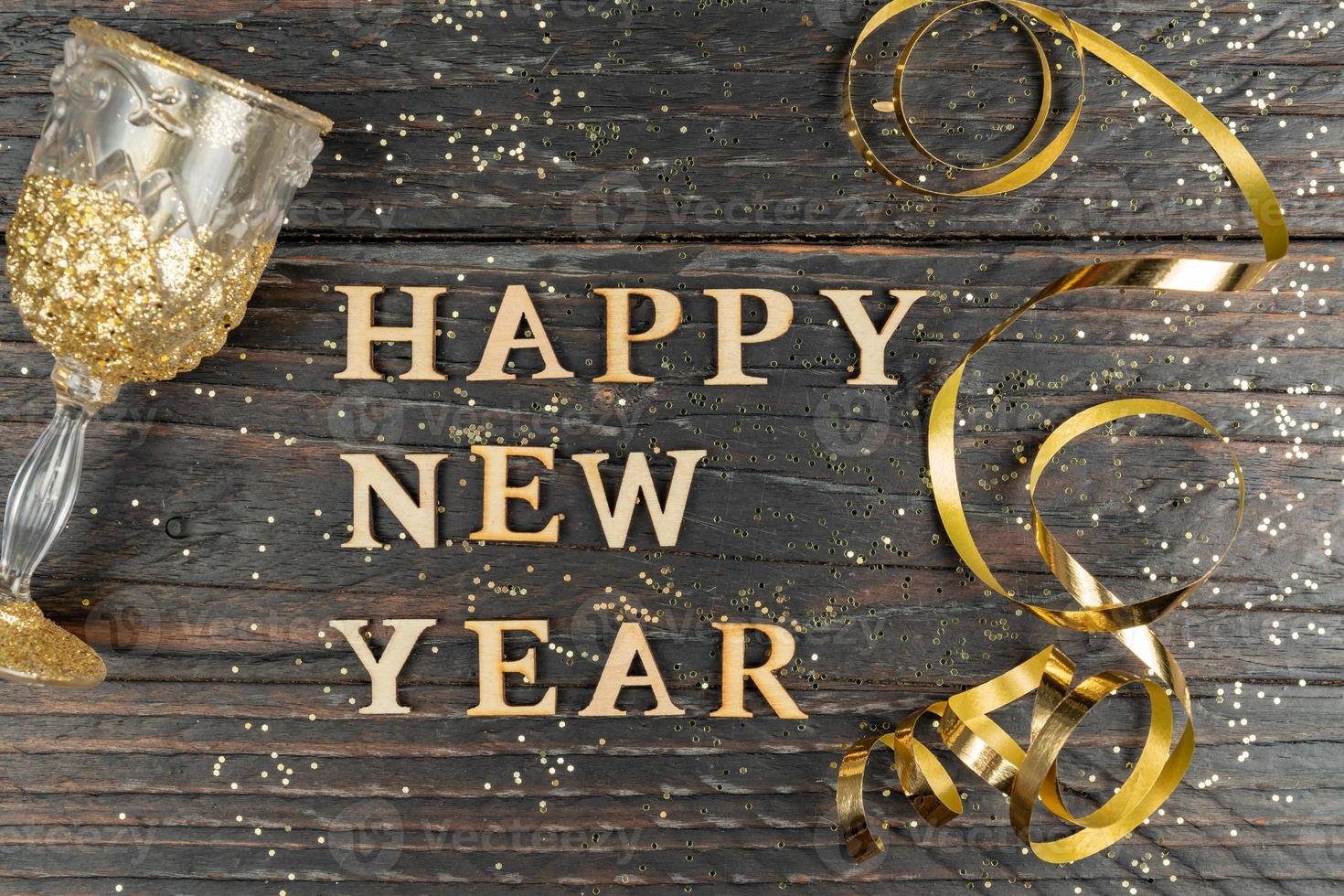 gelukkig nieuw jaar groet kaart. glas van Champagne en serpantine van goud kleur Aan houten tafel met verspreide confetti. foto