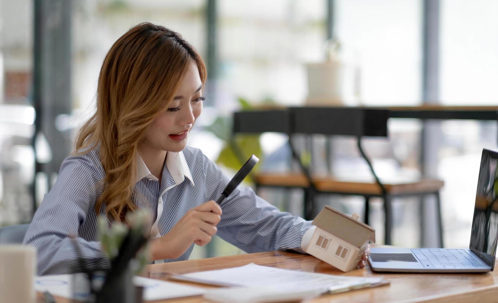 dichtbij omhoog van onderneemsters Holding vergroten glas vinden een houten vorm van een huis, makelaar, tussenpersoon, verzekering, ontwikkelaar, planning en investering echt landgoed bedrijf concept, foto