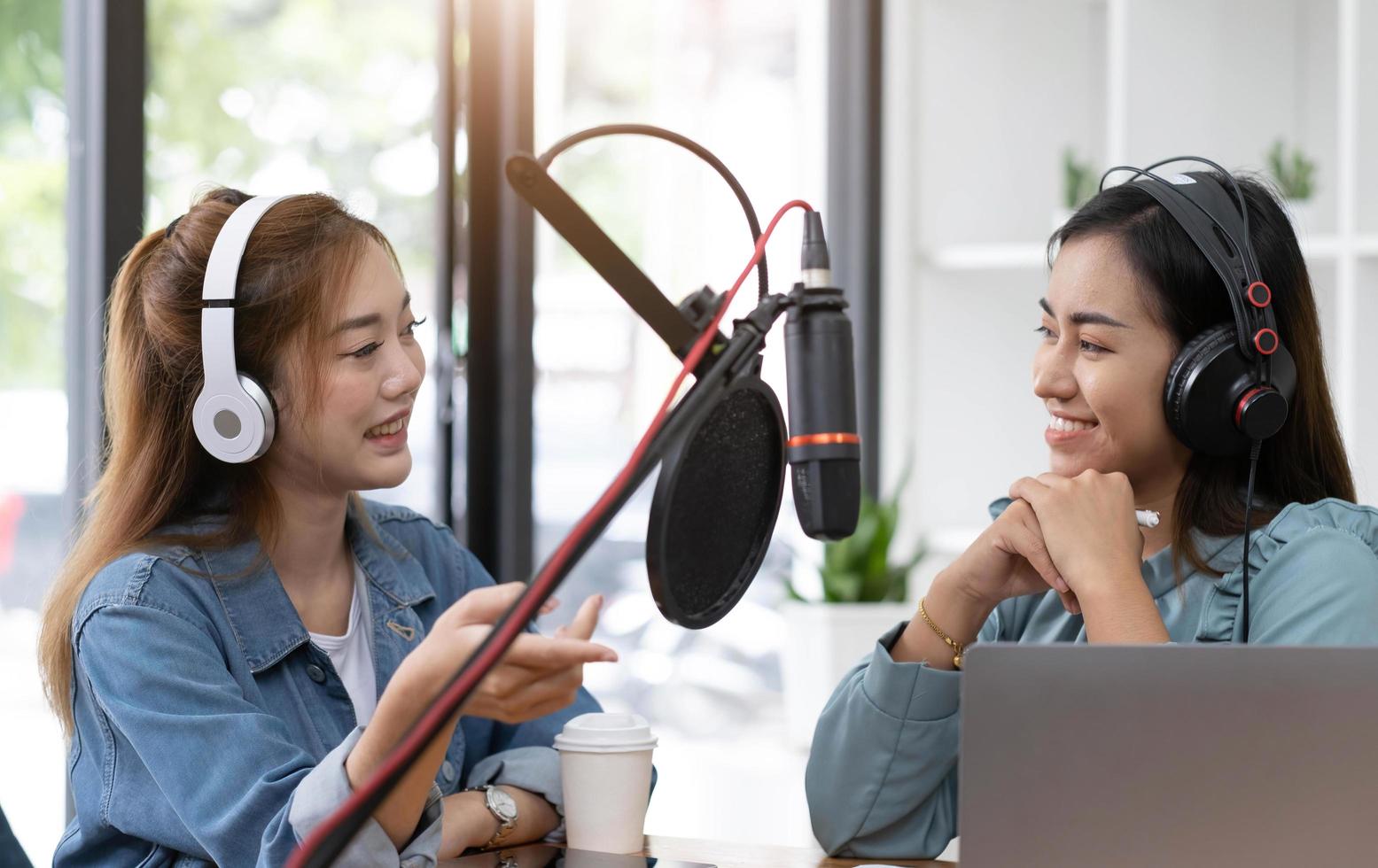 glimlach twee Aziatisch jong vrouw, Mens radio gastheren in koptelefoon, microfoon terwijl praten, gesprek, opname podcast in omroep Bij studio samen. technologie van maken Vermelding audio concept. foto