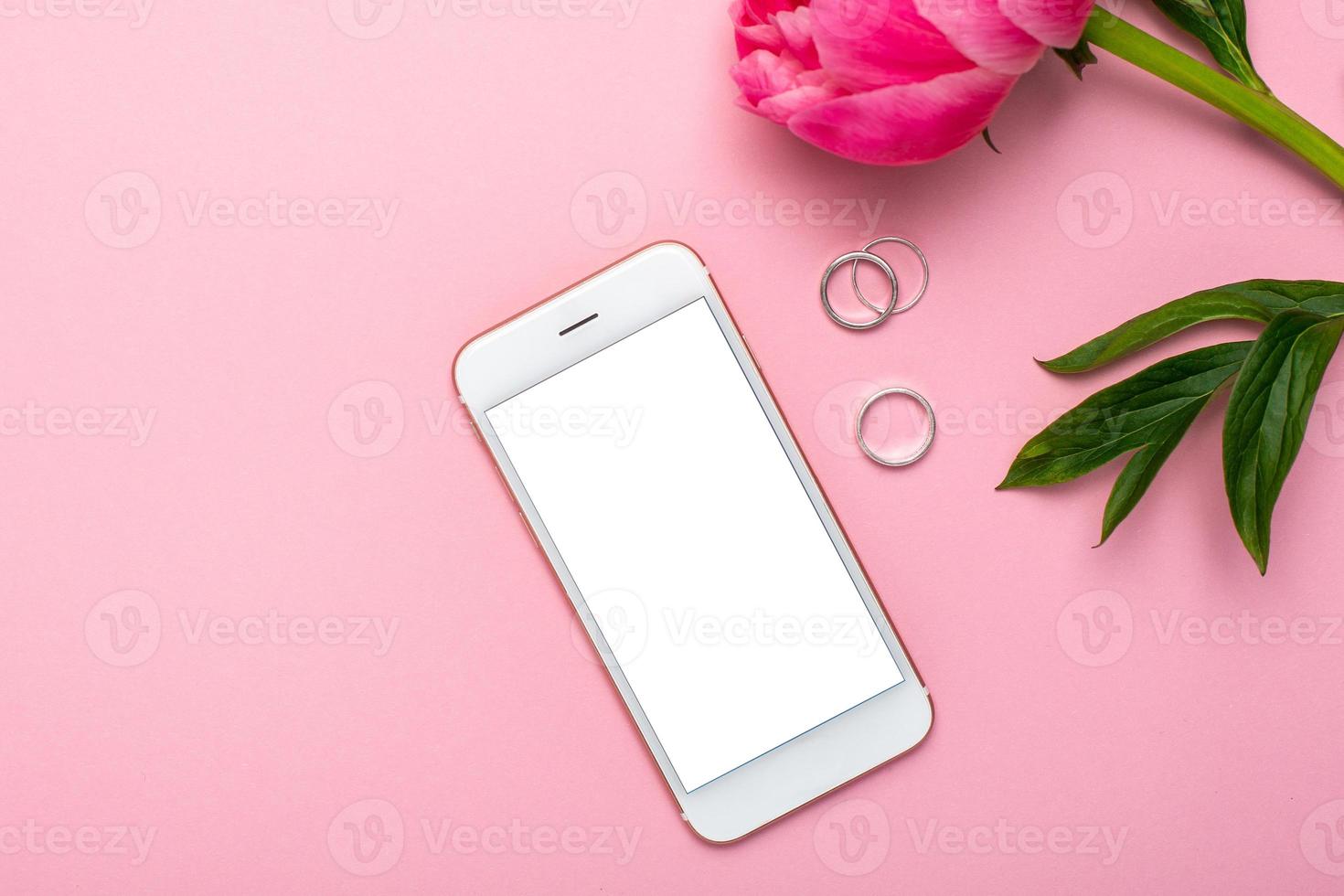 mobiel telefoon bespotten omhoog en pioen bloem Aan roze pastel tafel in vlak leggen stijl. vrouw werken bureau.zomer kleur foto