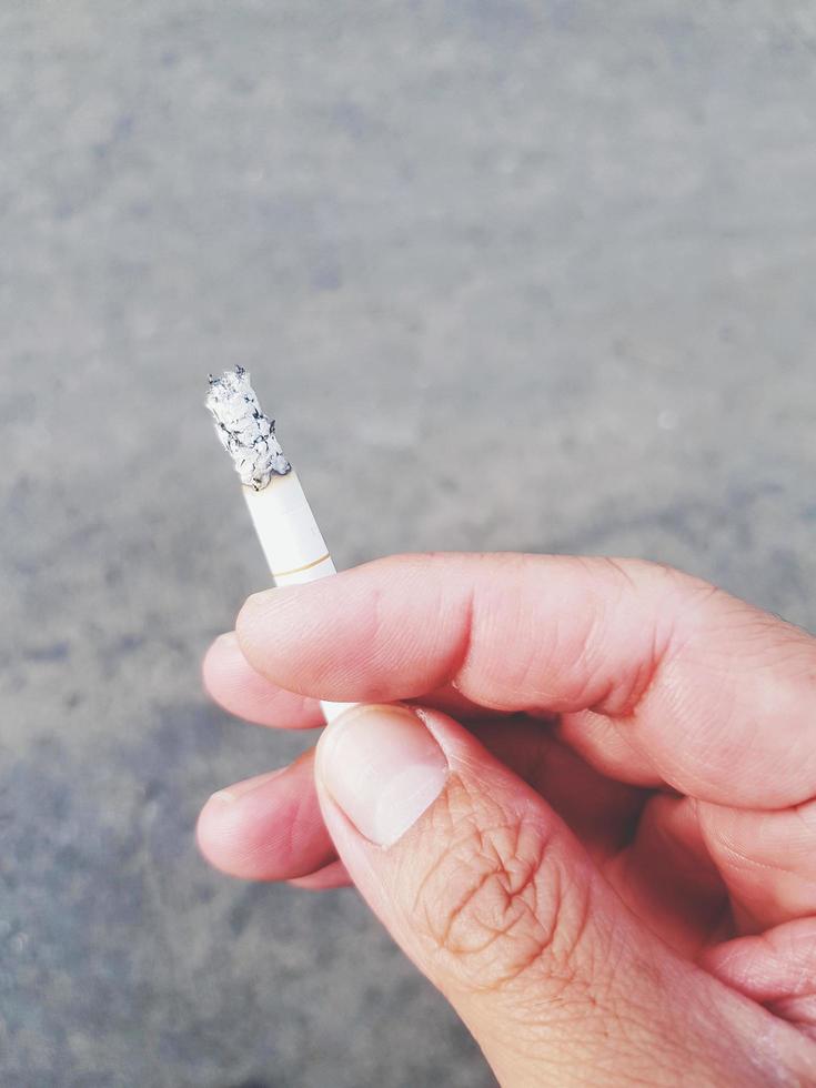 dichtbij omhoog hand- van Mens Holding sigaret met weg of straat achtergrond in wijnoogst toon. roken, slecht Gezondheid en kanker concept foto