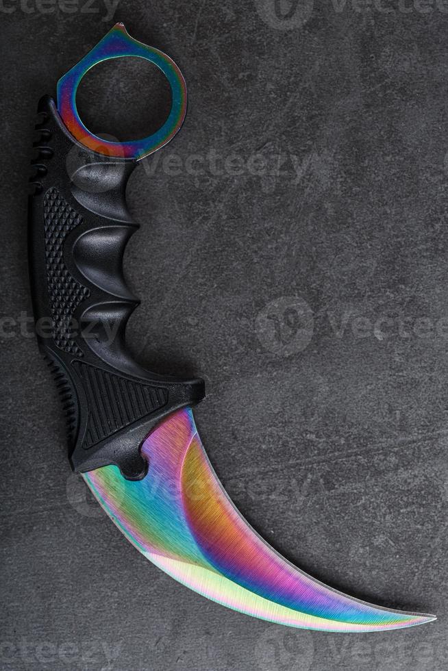 kerambit dolk met een regenboogkleurig blad Aan een donker getextureerde achtergrond. foto