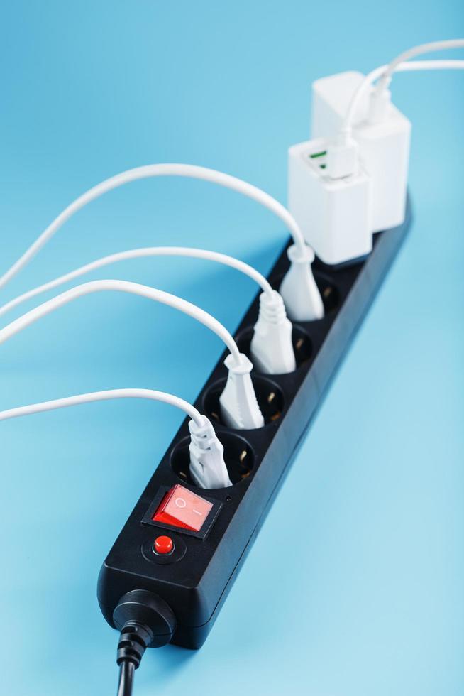 een zwart lichtnet filter met elektrisch verkooppunten ingevoegd in het met wit pluggen van elektrisch huishoudelijke apparaten Aan een blauw achtergrond foto